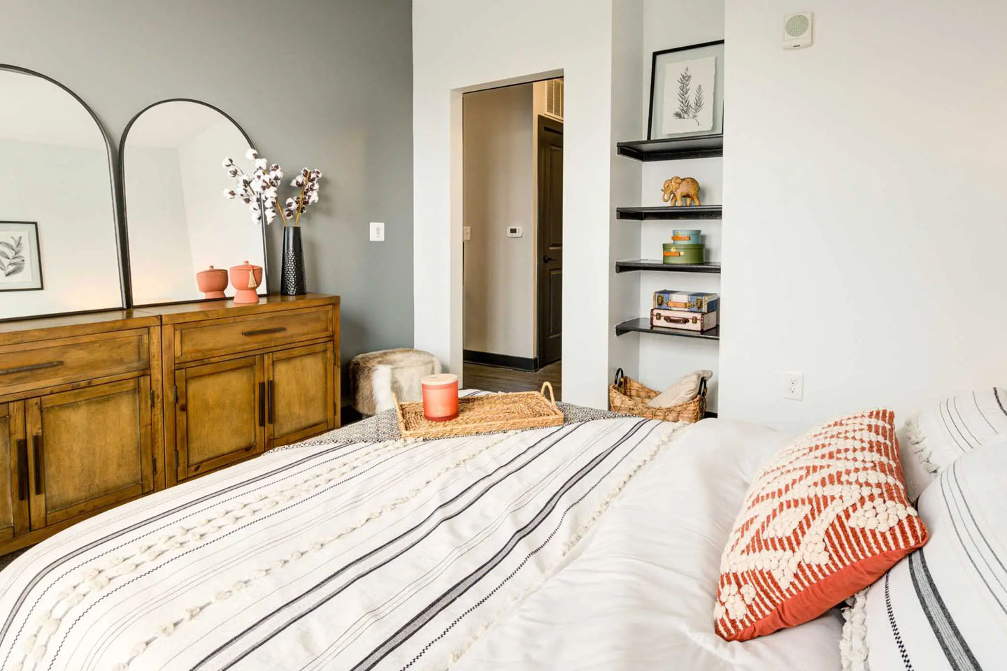 Bedroom with large rustic dresser and mirrors in front of a comfortably sized bed and shelving units.