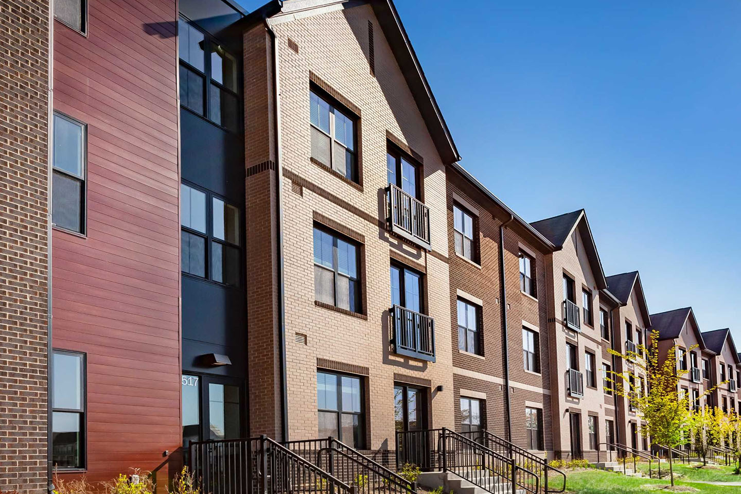 Red and brown colored apartment buildings with trees planted in front of them.